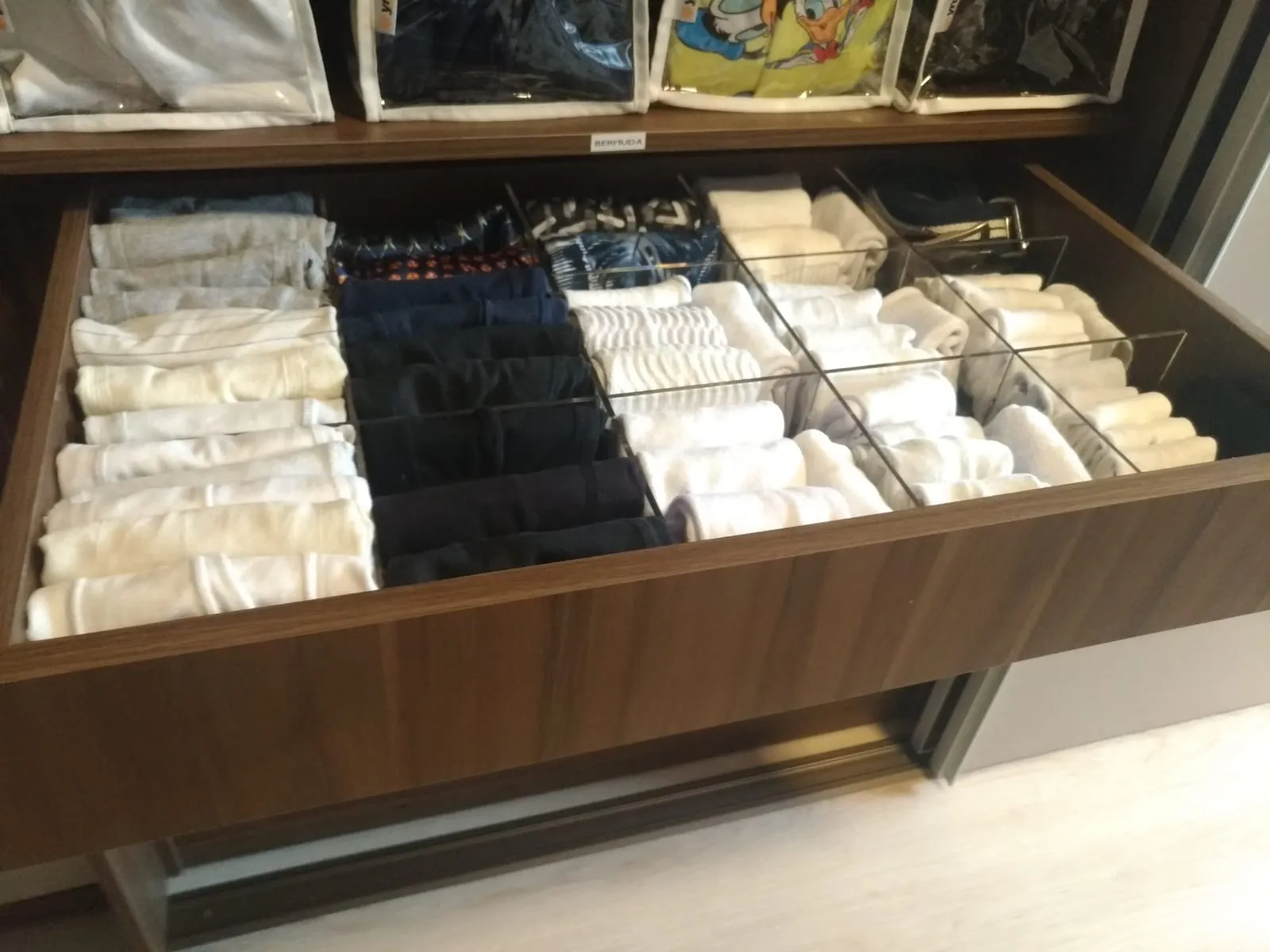 Cajón de vestidor dividido en compartimentos con ropa blanca, negra y beis doblada y agrupada por tono.