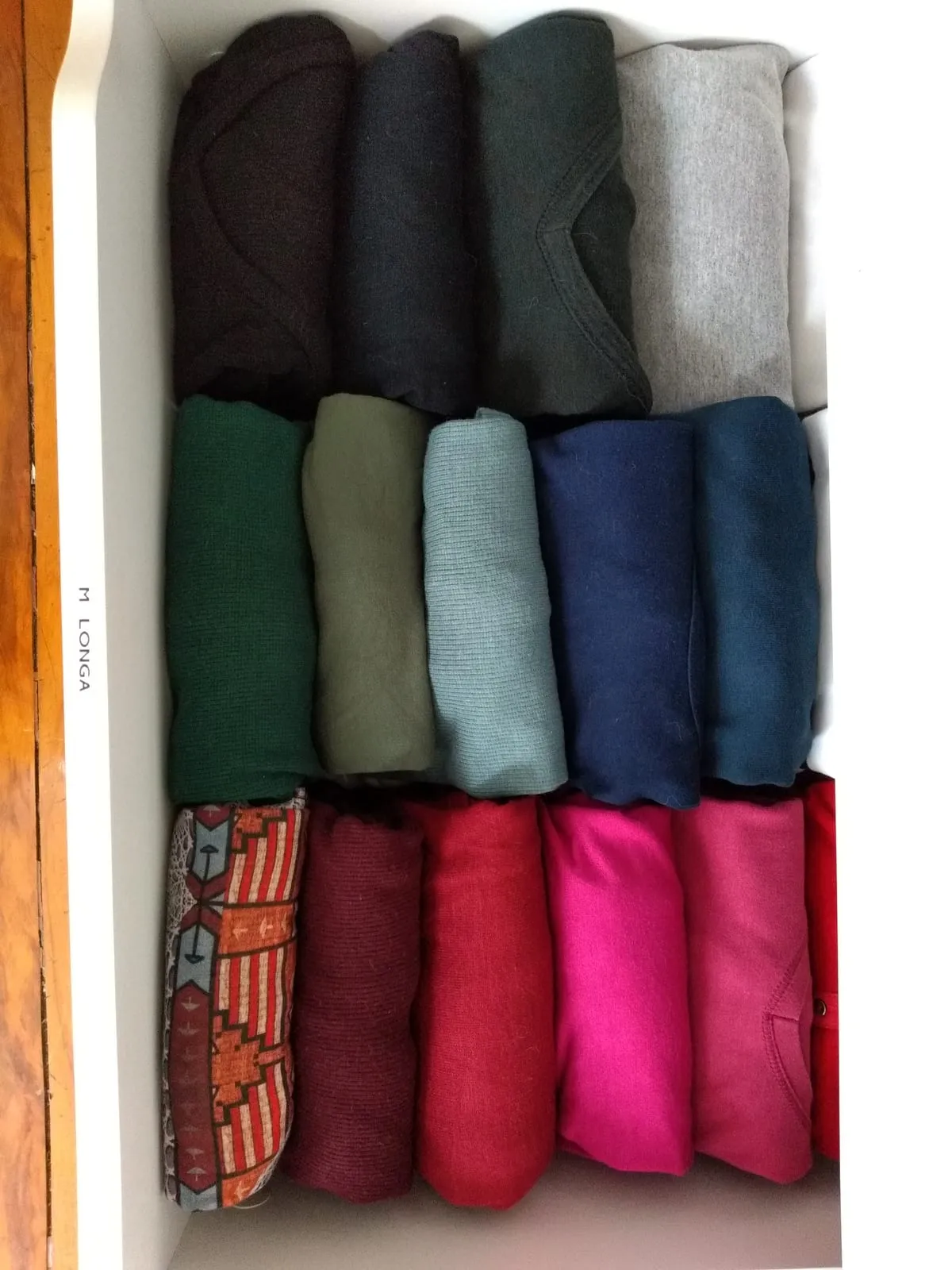 Jerséis doblados en vertical y colocados en tres filas por color, de los oscuros a los rojos y rosas.