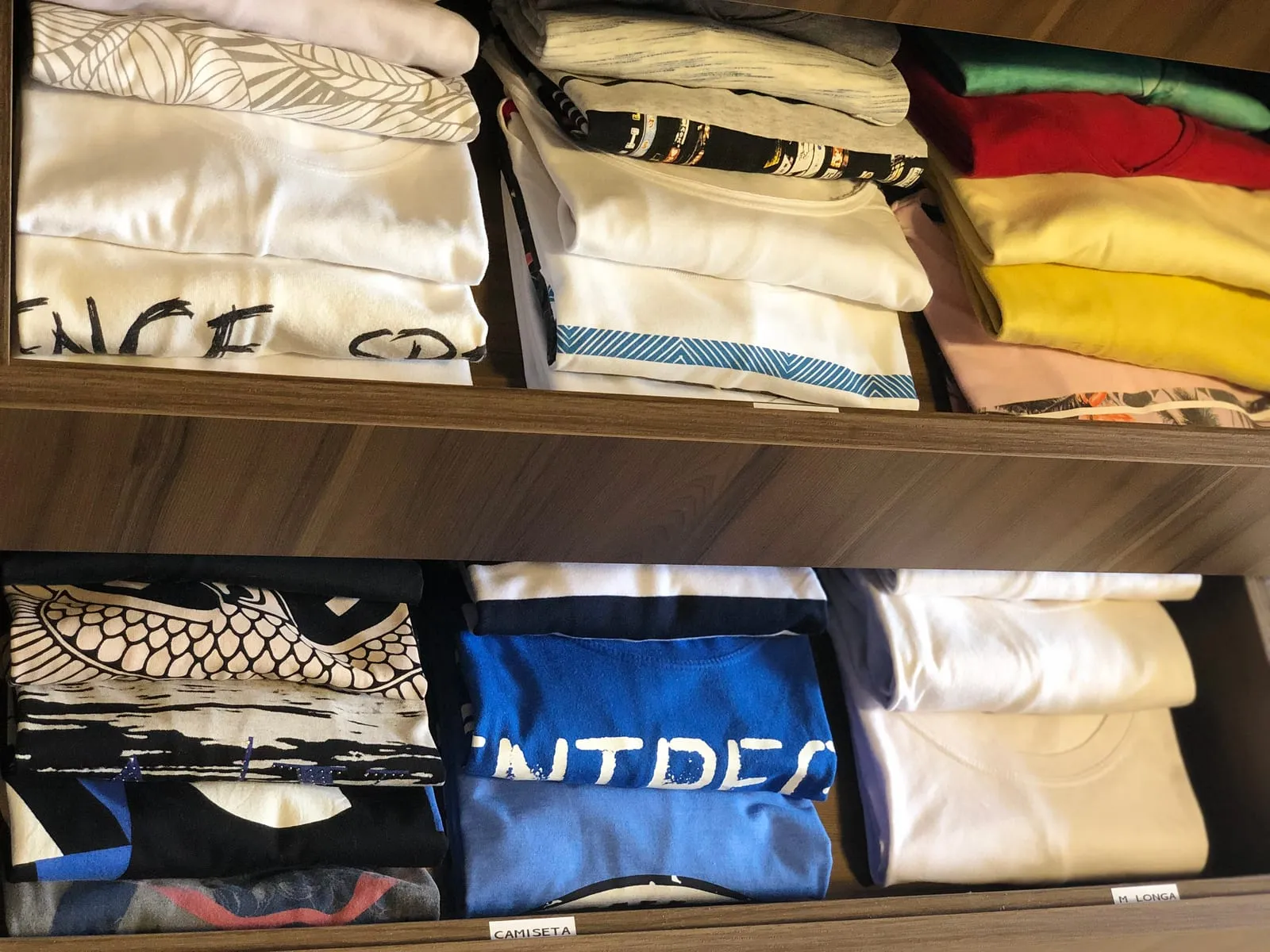 Baldas con camisetas dobladas del mismo tamaño y agrupadas por color y estampado.