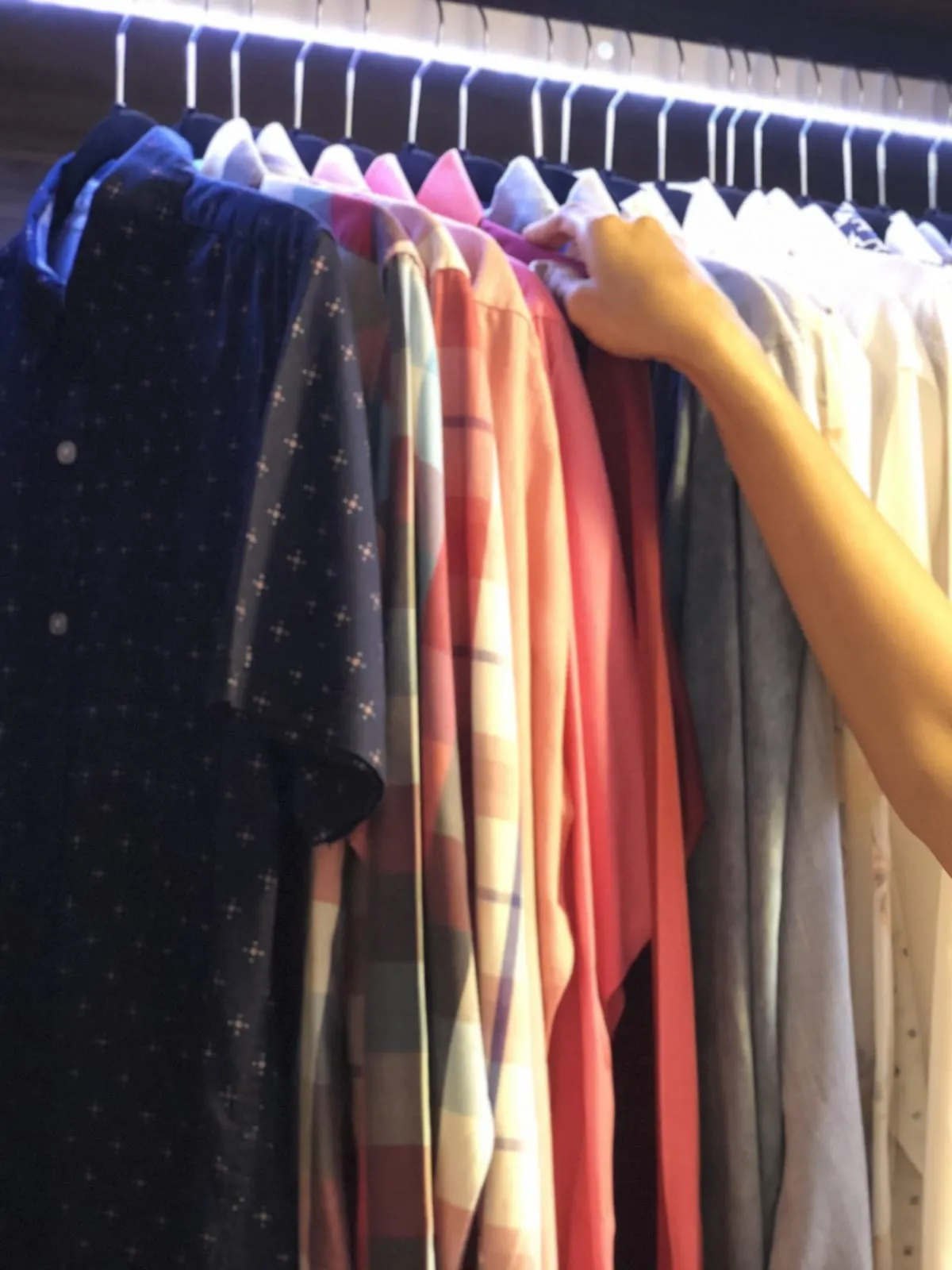 Camisas y vestidos colgados por color en una barra con luz, con la ropa lisa y la estampada separadas.