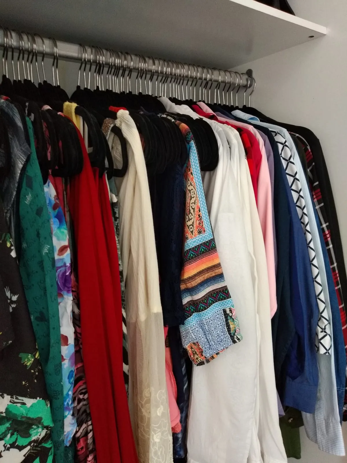 Barra de armario con blusas y vestidos colgados en perchas iguales y agrupados por color.