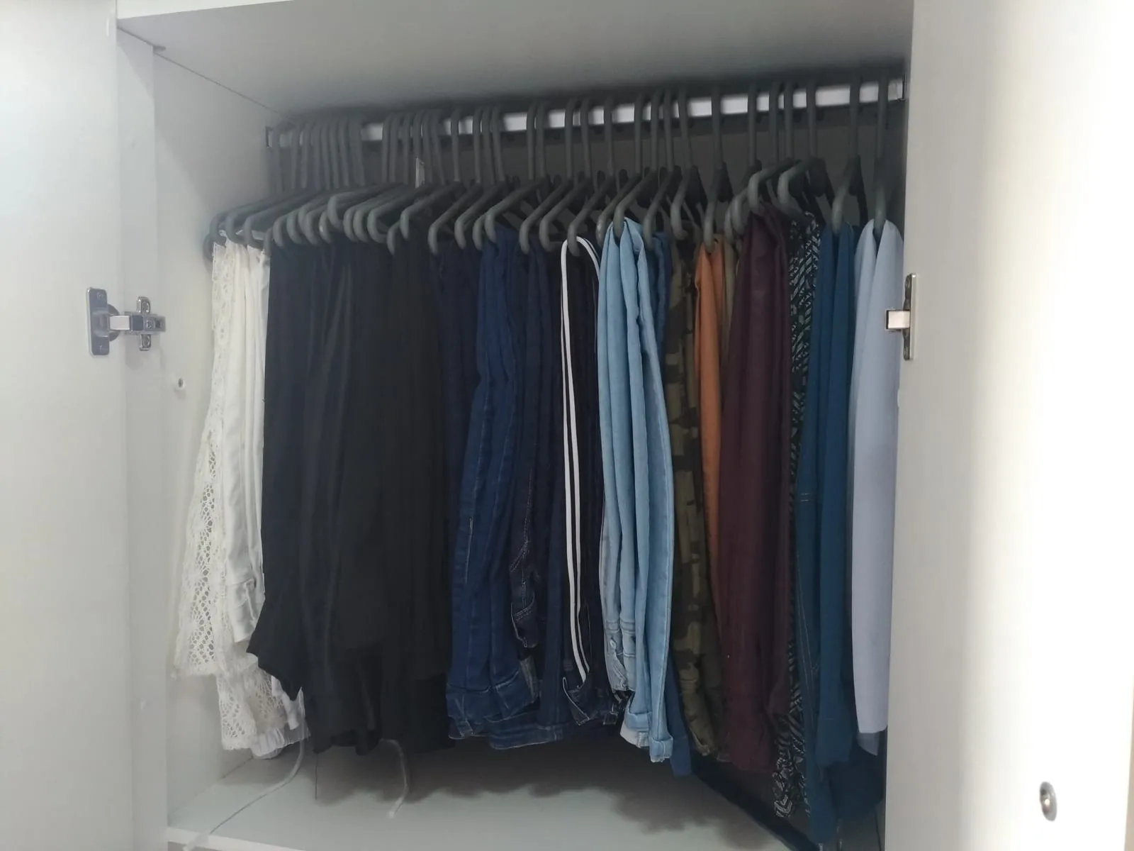Barra de armario con pantalones colgados en perchas iguales y ordenados del claro al oscuro.