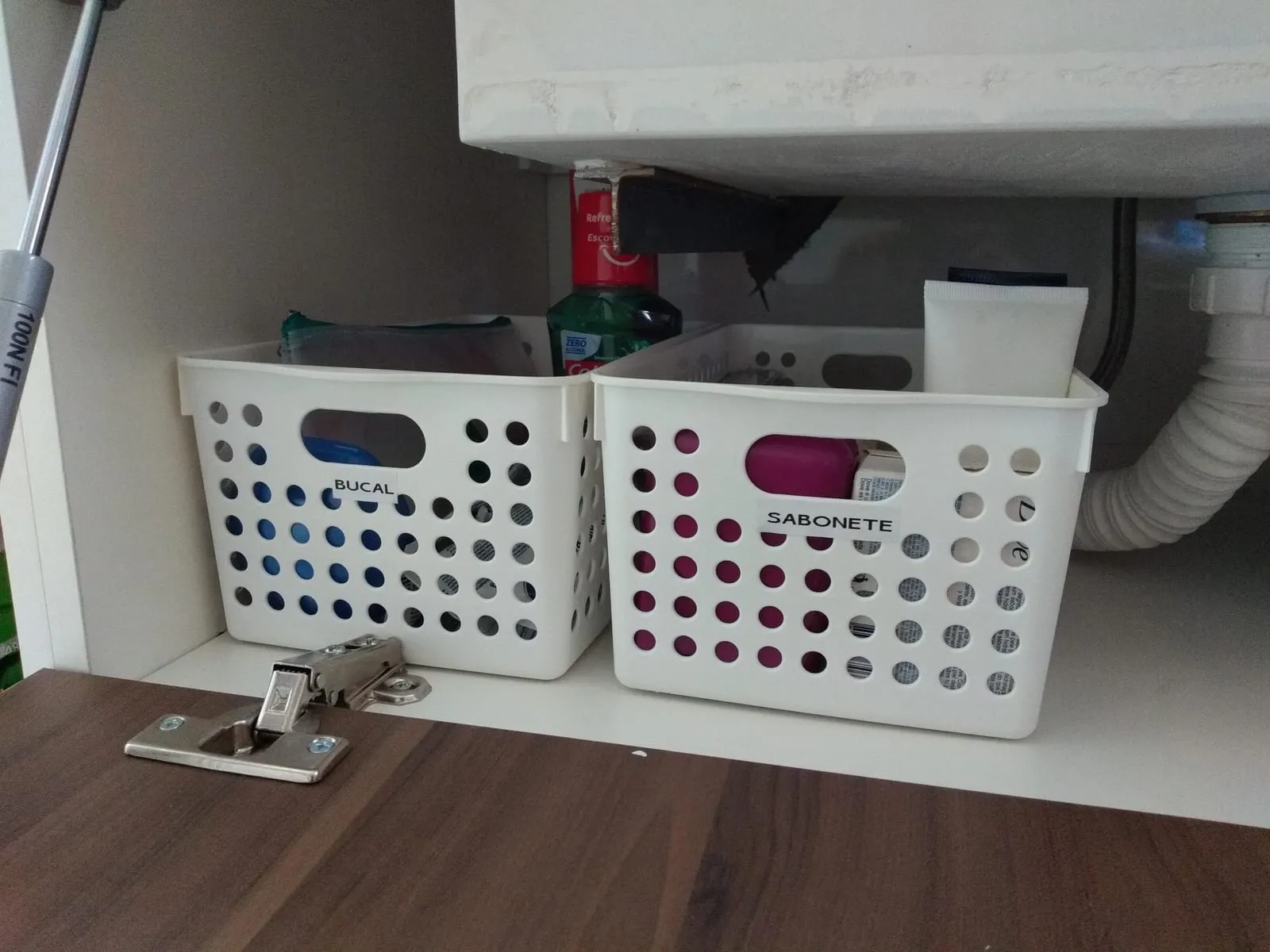 Hueco bajo el lavabo aprovechado con dos cestas blancas etiquetadas.