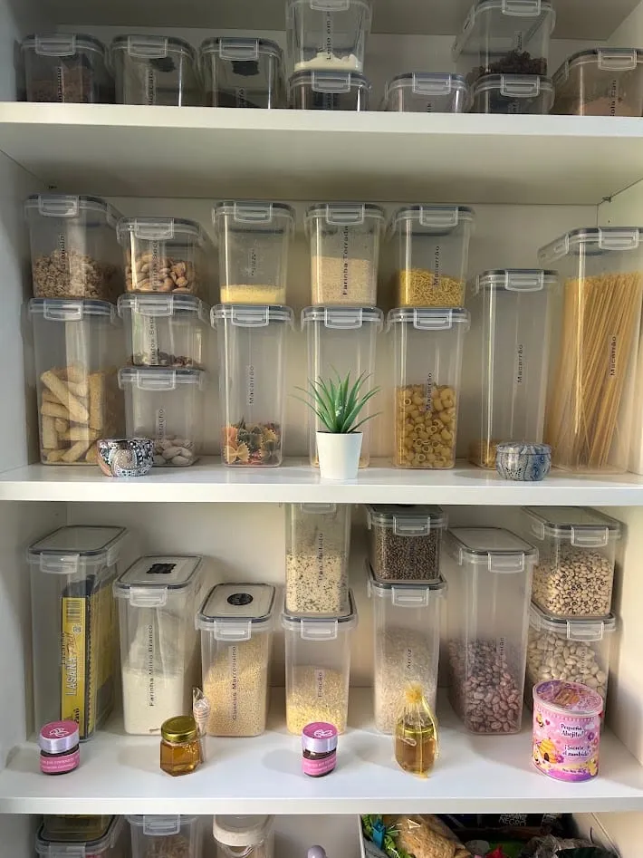 Despensa con botes herméticos transparentes alineados en cuatro baldas, cada alimento a la vista.