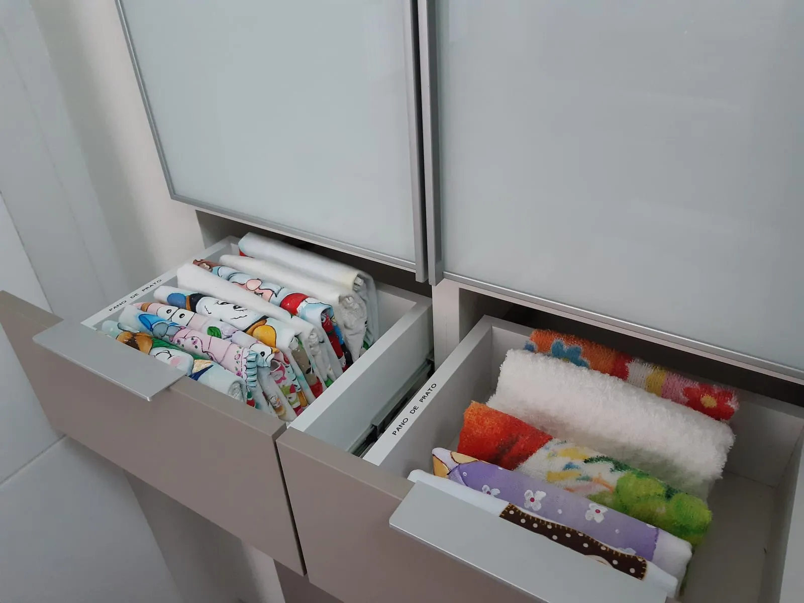 Cajones de cocina etiquetados con los paños doblados en vertical, uno junto a otro.