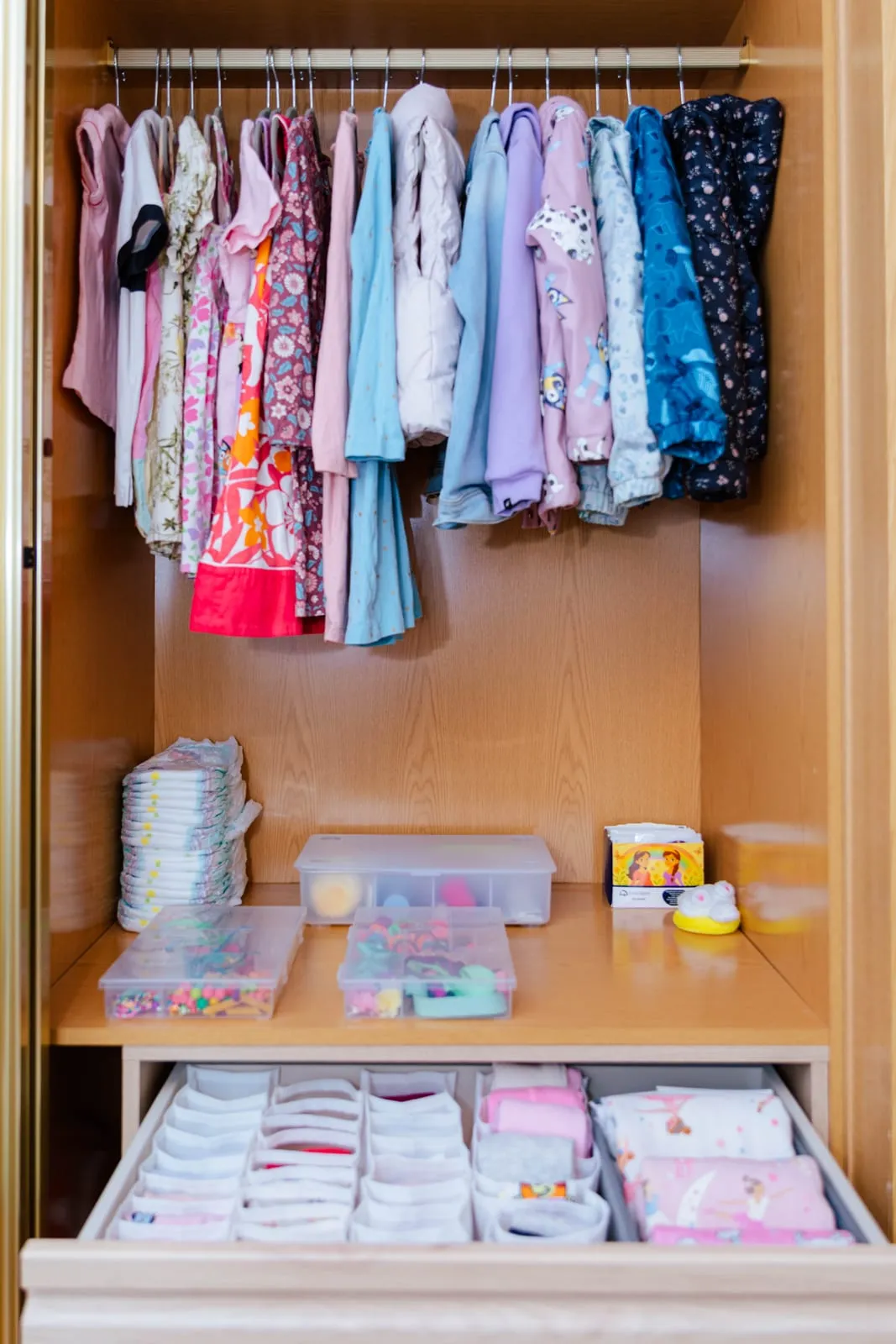 Armario infantil con la ropa colgada por color, cajas organizadoras en la balda y un cajón con separadores para la ropa doblada.